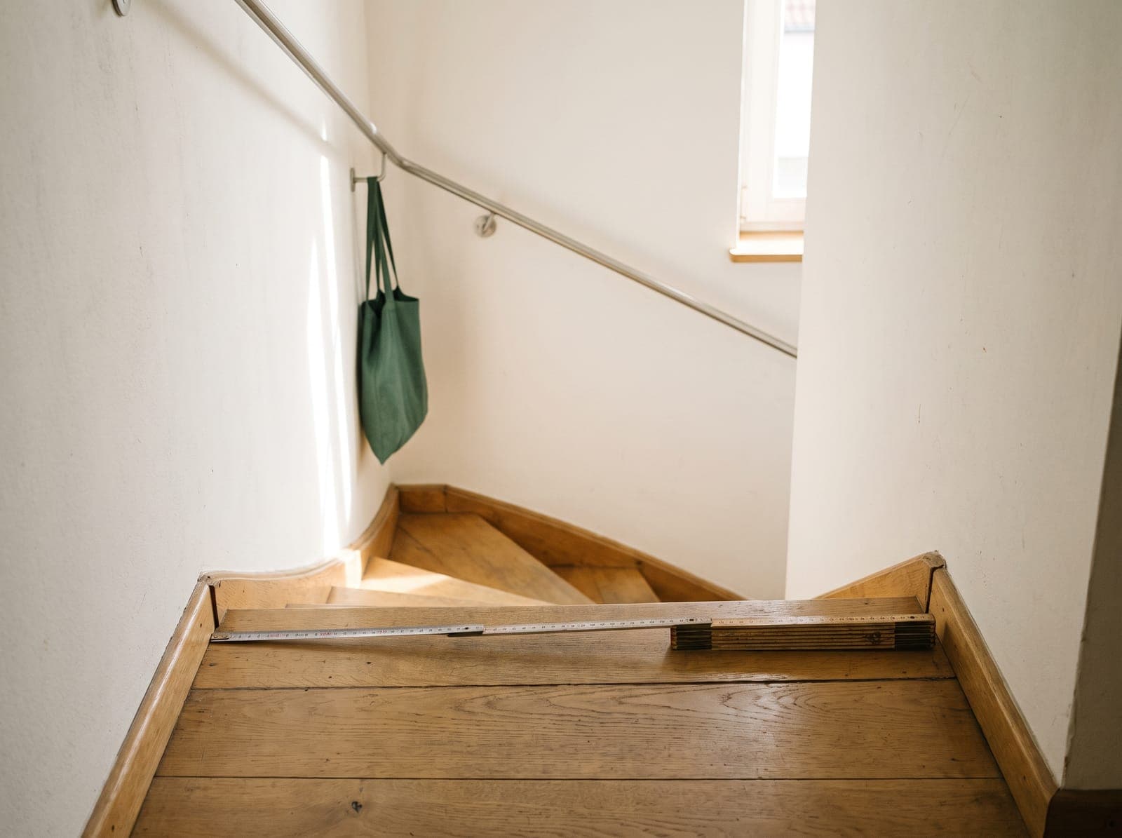 Zollstock und Maßband liegen quer auf der obersten Stufe einer schmalen gewendelten Holztreppe